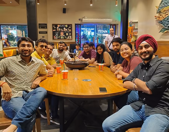 Group of ten people sitting around a wooden table in a restaurant with drinks and smartphones.