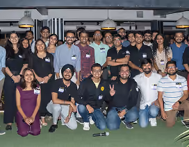Group of diverse people posing indoors on green carpet, smiling for a group photo.